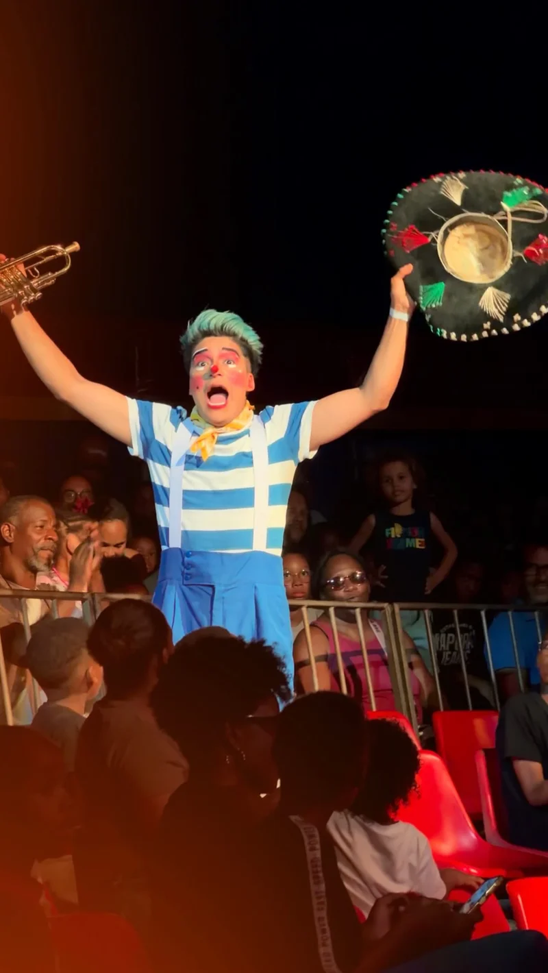 Artista del circo con sombrero y trompeta frente al público.